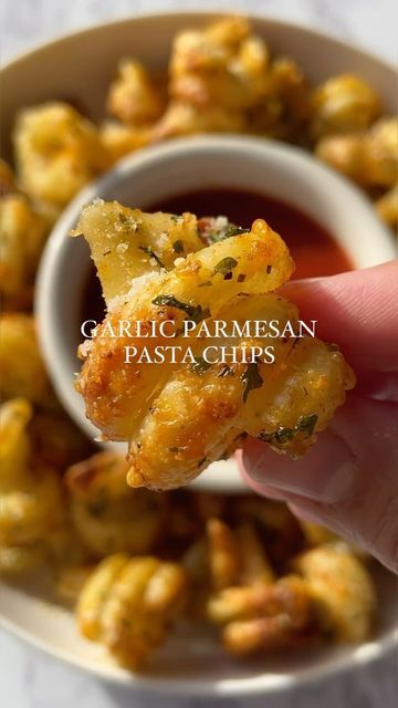 someone is holding up some food in their hand with the words garlic parmesan pasta chips