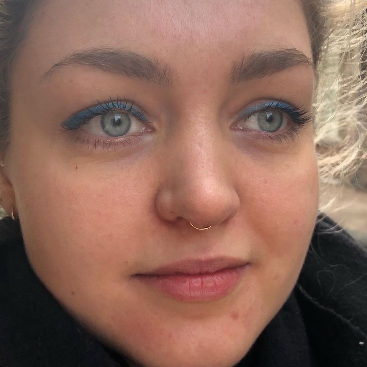 a close up of a woman with blue eyes and nose piercings on her nose