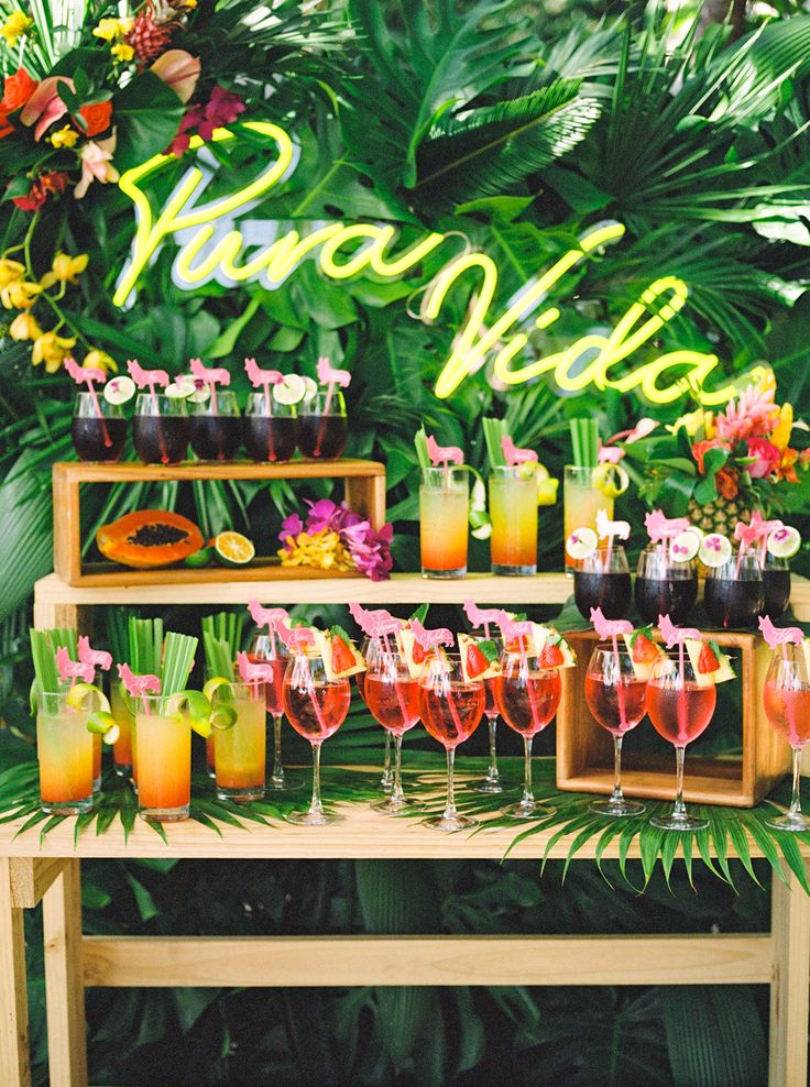 there are many glasses on the table with drinks in front of them and flowers behind it