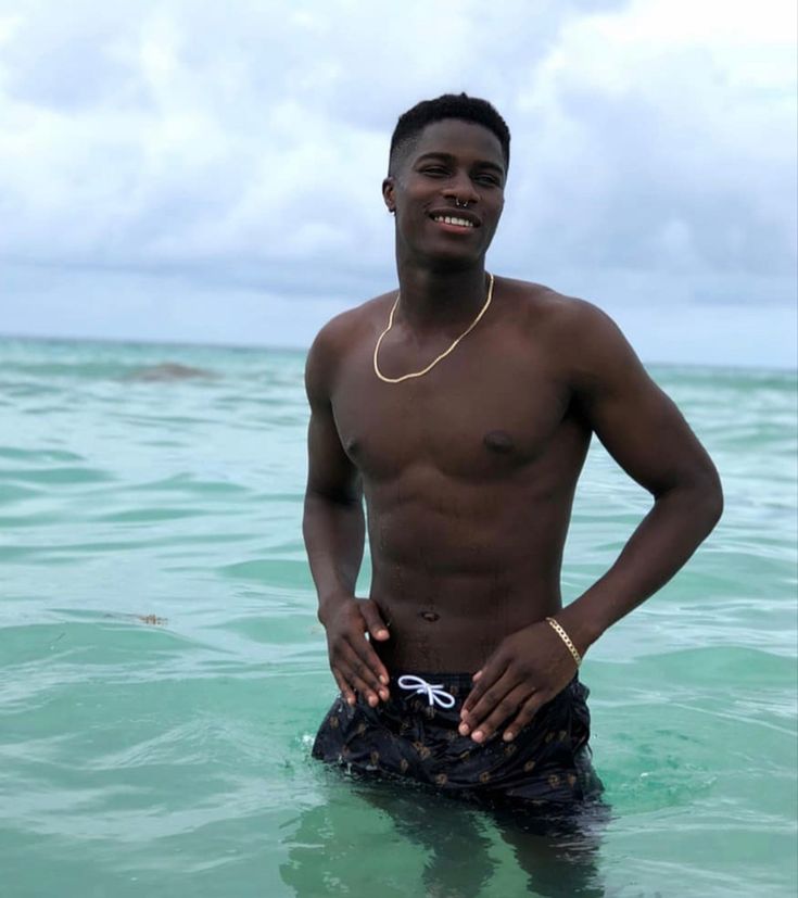 a young man standing in the ocean with his hands on his hips and smiling at the camera