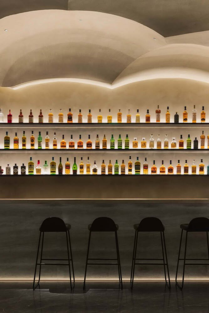 three stools in front of a bar with bottles on the wall and shelves behind them