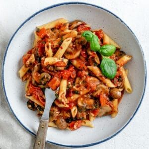 a white plate topped with pasta covered in tomato sauce and spinach sprinkled on top