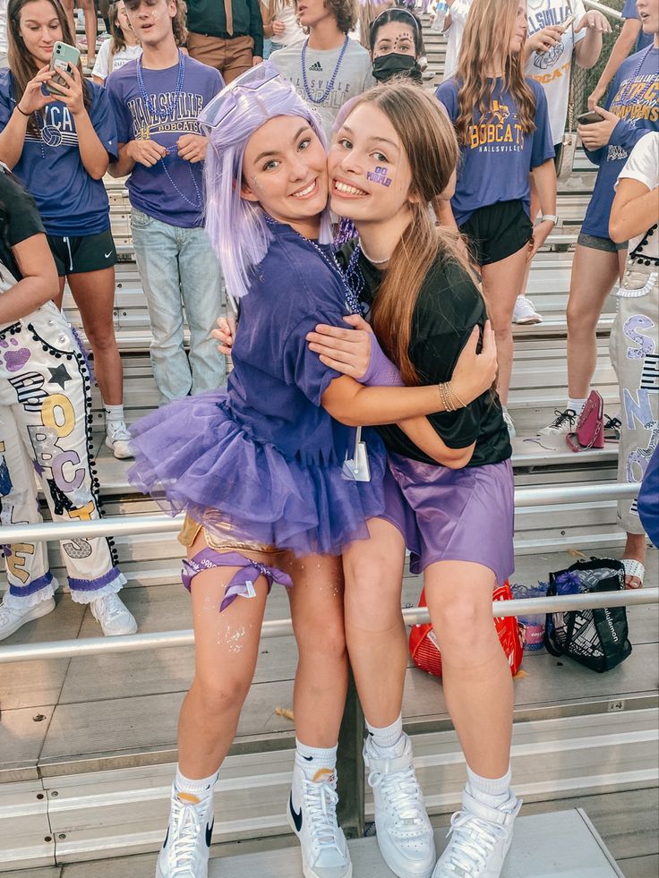 two girls hugging each other in front of some fans at a sporting event with their faces painted purple