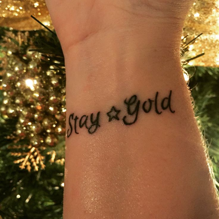 a woman's wrist with the word stay gold written on it and a christmas tree in the background