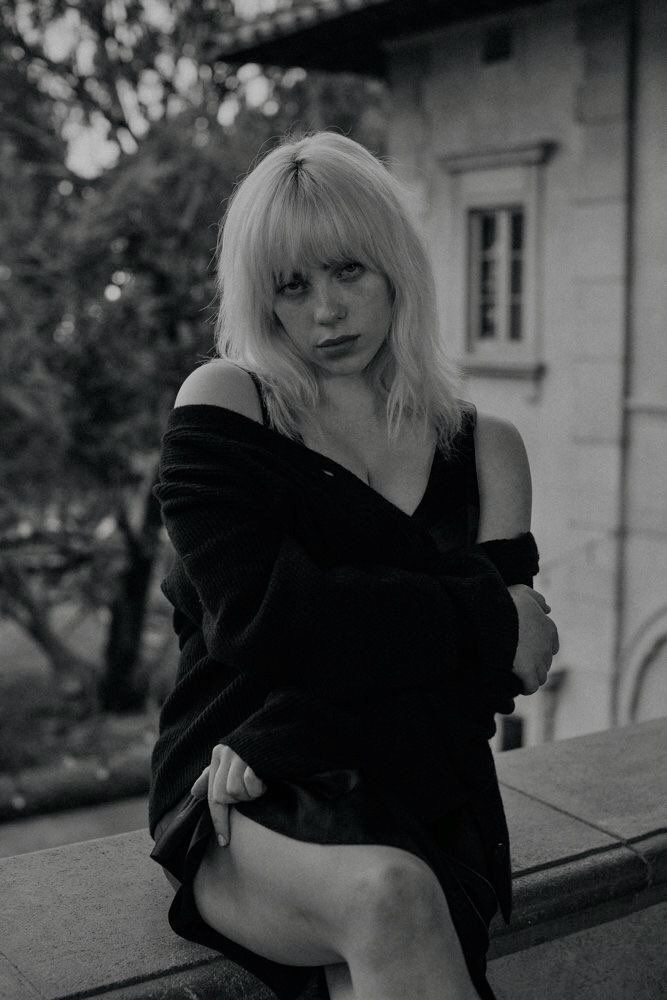 a black and white photo of a woman sitting on a ledge with her legs crossed