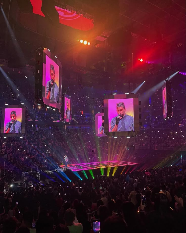 an audience at a concert with large screens on the wall and lights in front of them