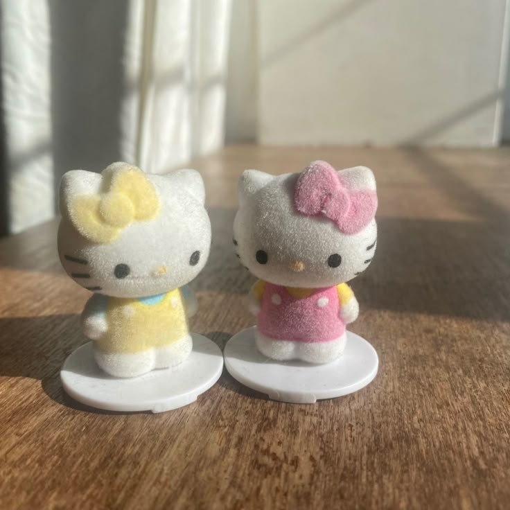 two hello kitty figurines sitting on top of a wooden table