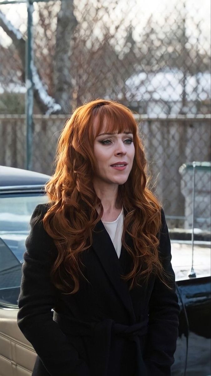 a woman with red hair standing in front of a car