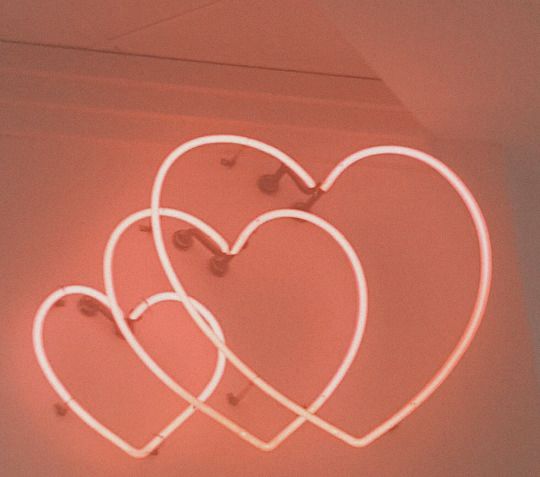 three heart shaped neon signs hanging from the side of a wall in front of a red background