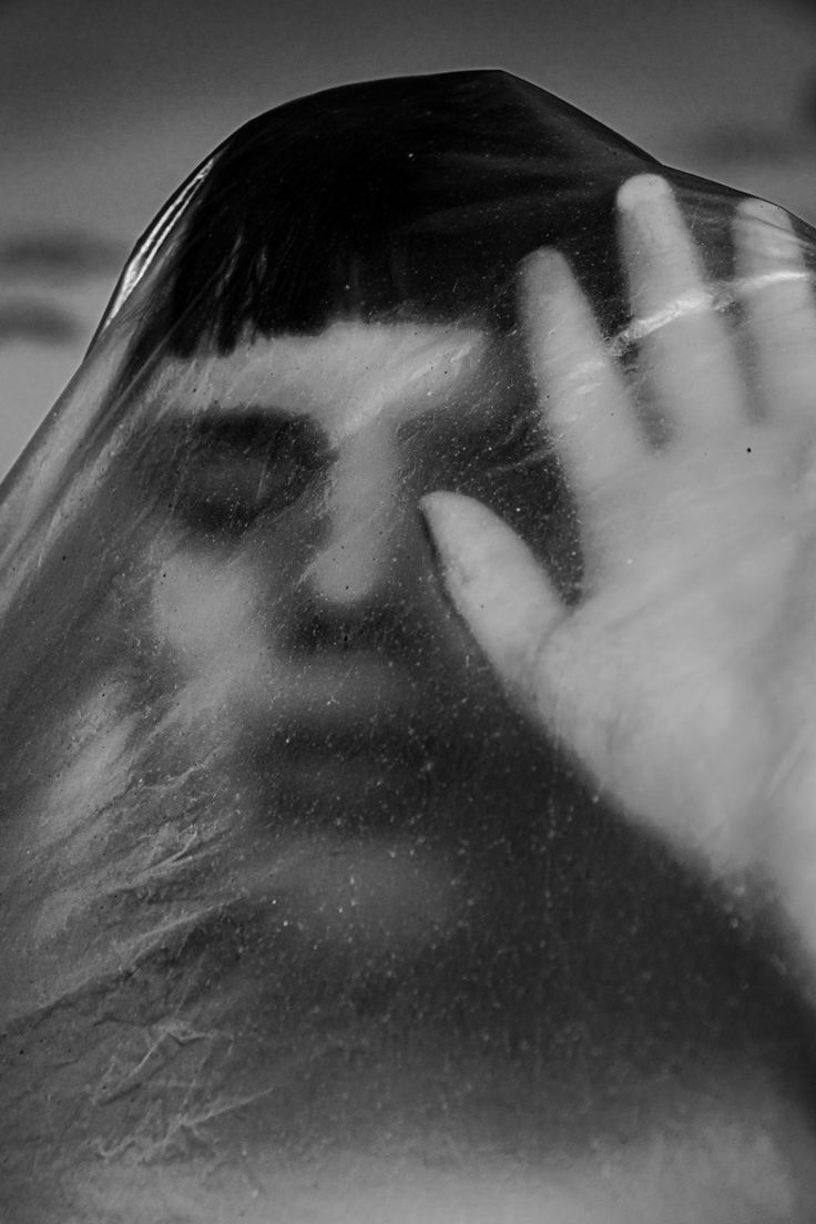 a person with their hand up to their face in front of a glass window that shows the reflection of someone's head