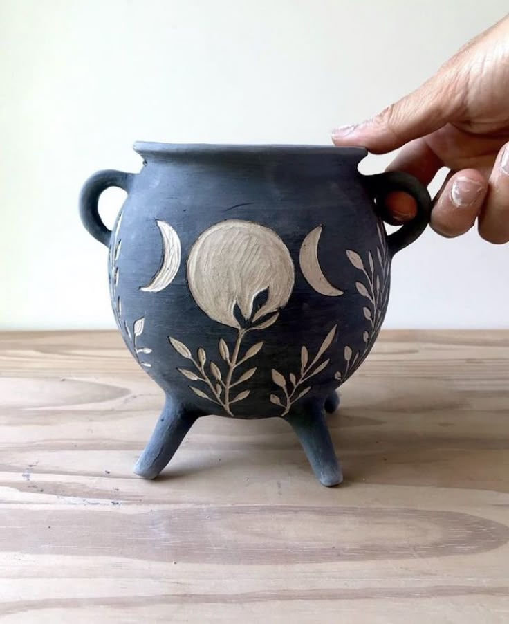 a hand is holding the handle of a black vase