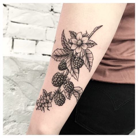 a woman's arm with blackberries and flowers on the left side of her arm