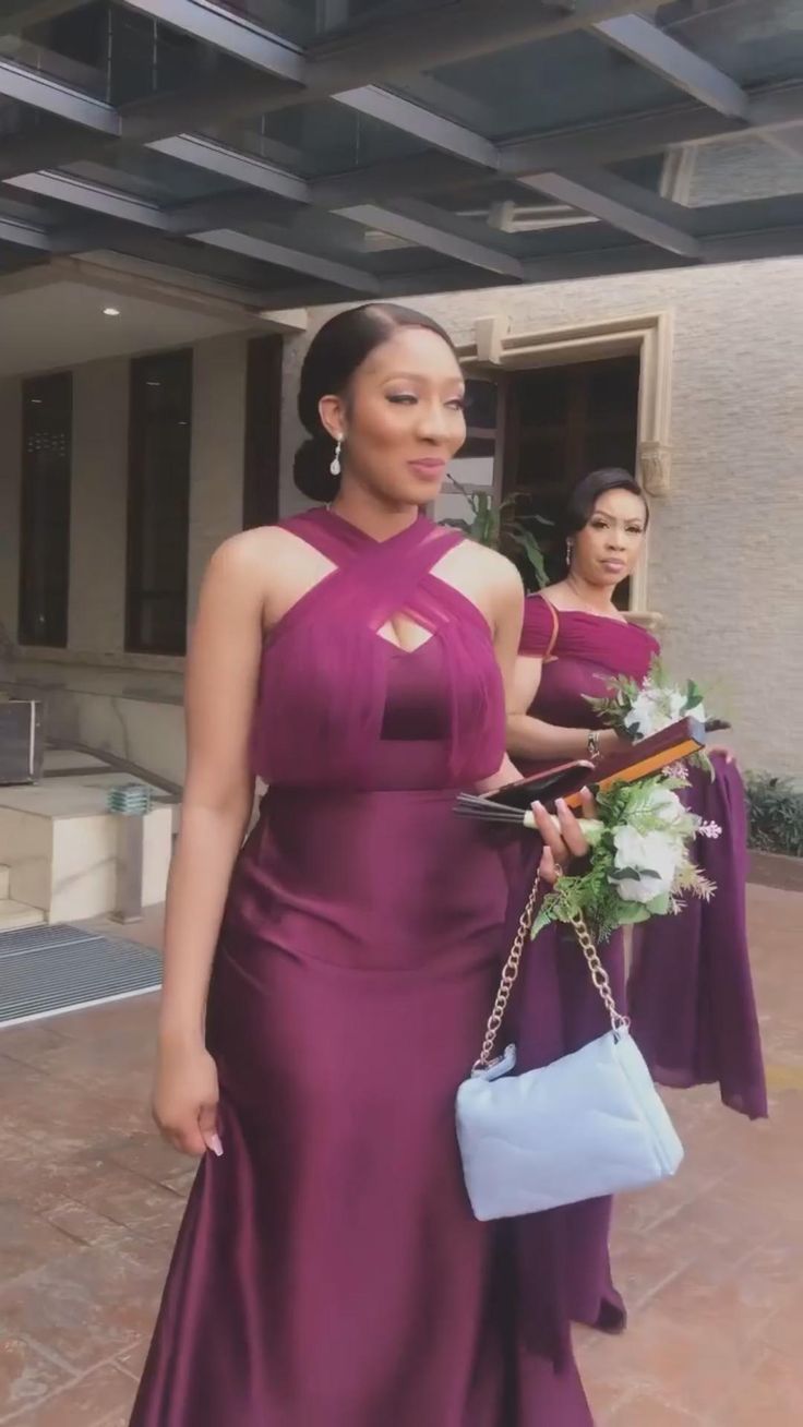 a woman in a long purple dress holding a purse and standing next to another woman