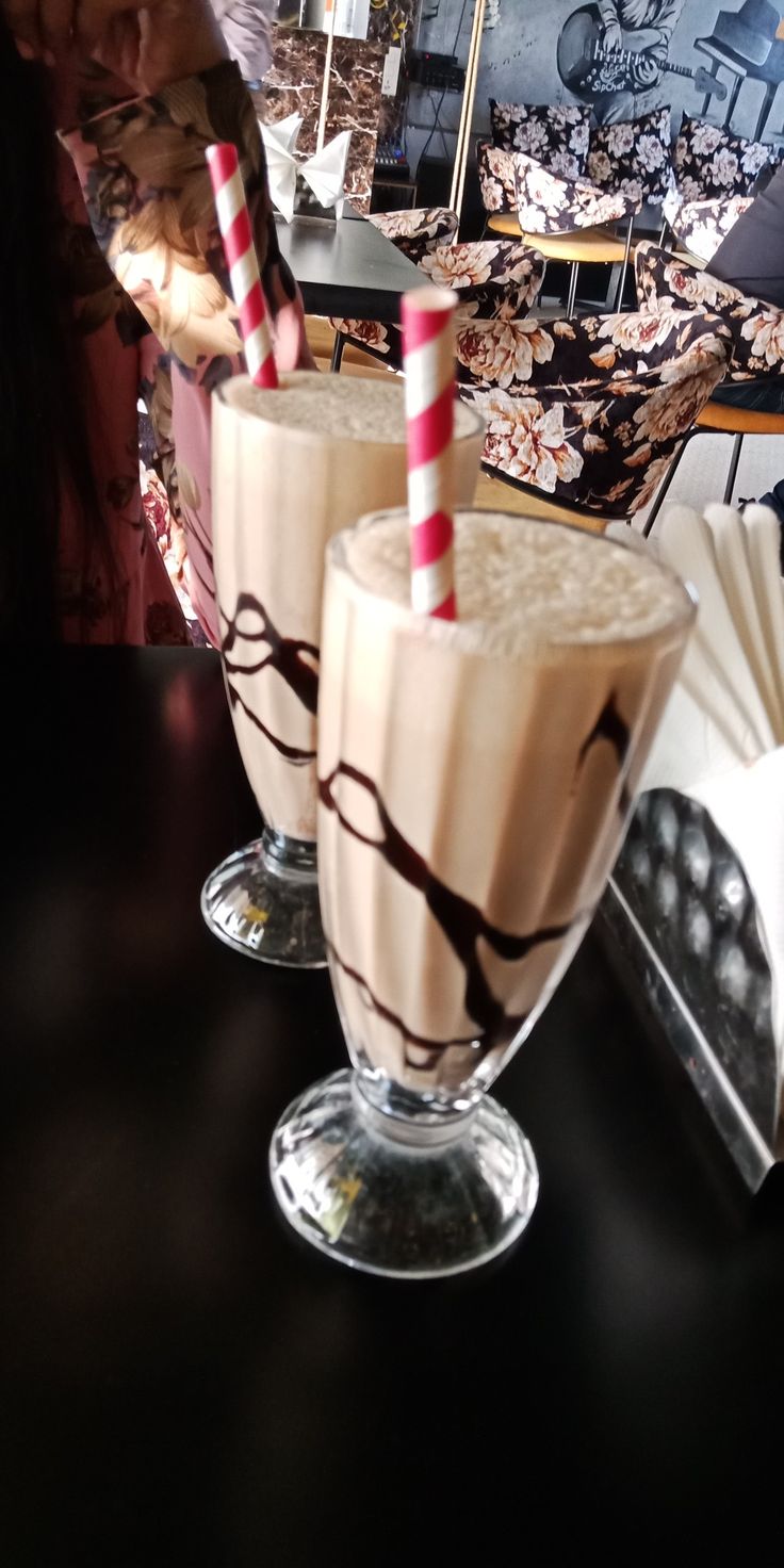 two glasses filled with milkshakes sitting on top of a table next to each other