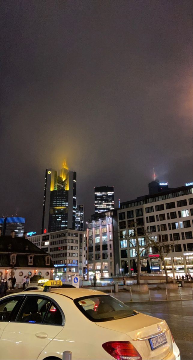 a white car parked on the side of a road in front of tall buildings at night