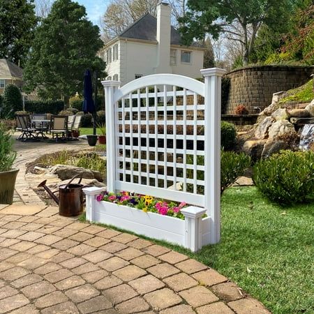 a white garden trellis sitting on top of a brick walkway next to a lush green yard