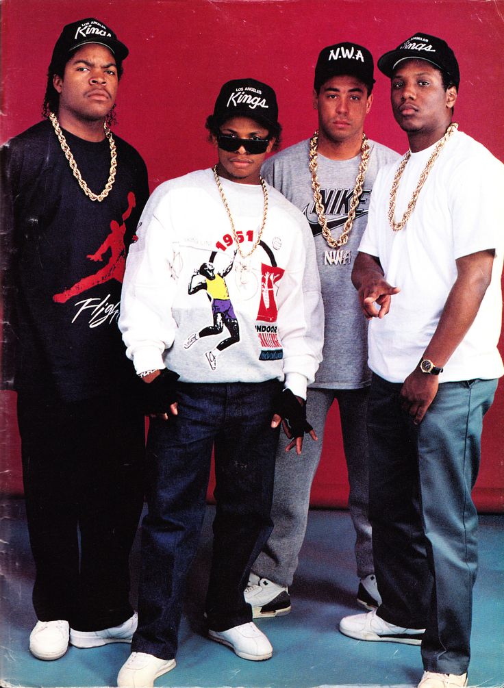 three men standing next to each other in front of a red wall wearing hats and sunglasses