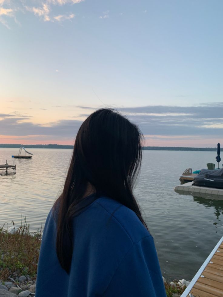 a woman is looking out over the water at boats in the distance and people standing on the dock