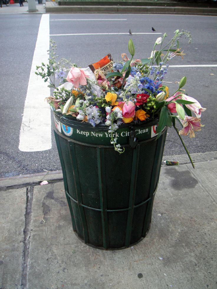 a trash can filled with flowers on the sidewalk