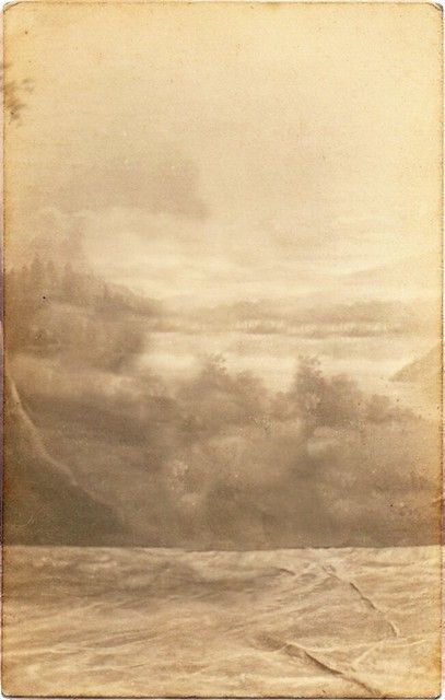 an old photo of the ocean with clouds in the sky and trees on the shore