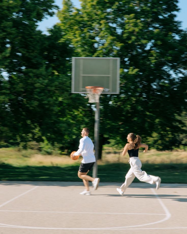 two people playing basketball on a court with trees in the background