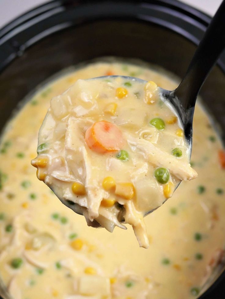 a spoon full of soup with peas, carrots and chicken in it is being held up