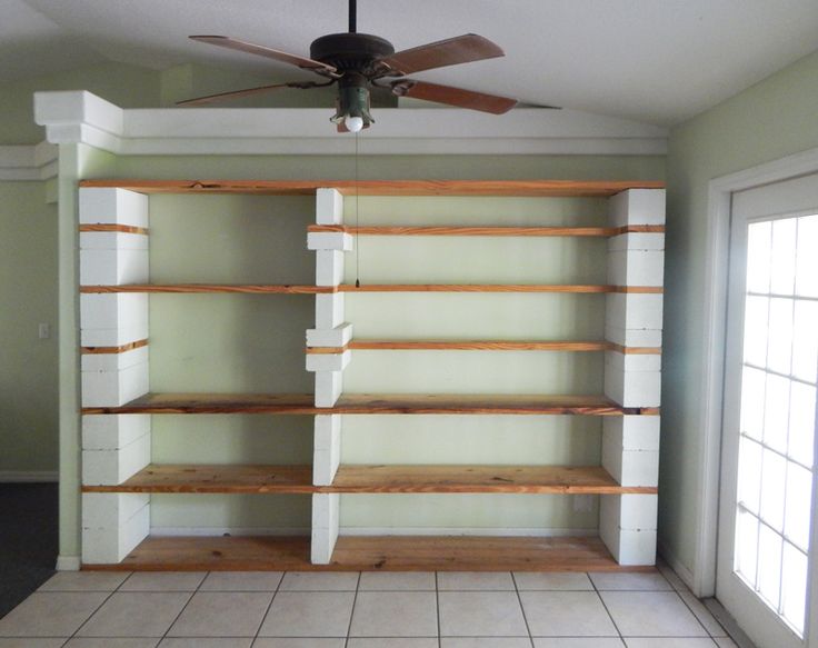 an empty room with some shelves and a ceiling fan in the corner, all white tile flooring