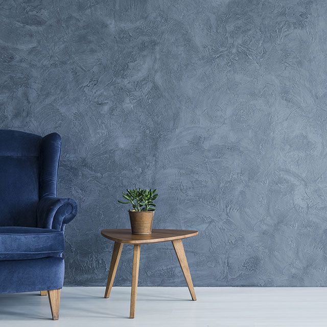 a blue chair next to a small table with a potted plant on it in front of a gray wall