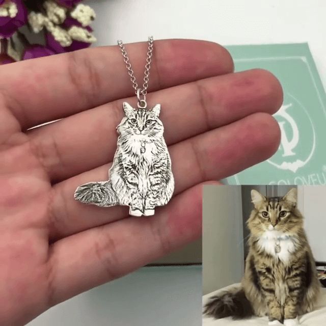 a hand holding a cat necklace in front of an image of it's face