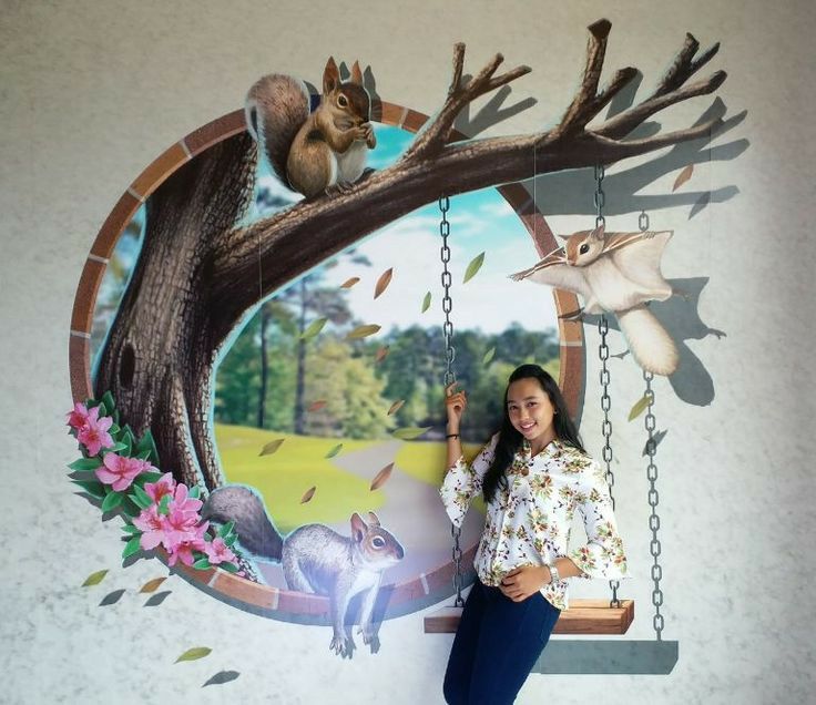 a woman standing in front of a mural with animals on the tree branch and squirrels