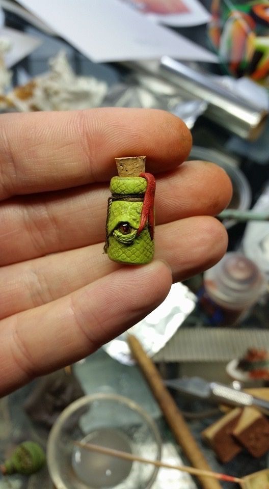 a hand holding a tiny green object with a red eye on it's face