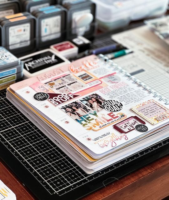 an open planner book sitting on top of a wooden table next to other papers and pens