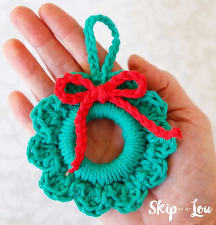 a hand holding a crocheted ornament with a red bow