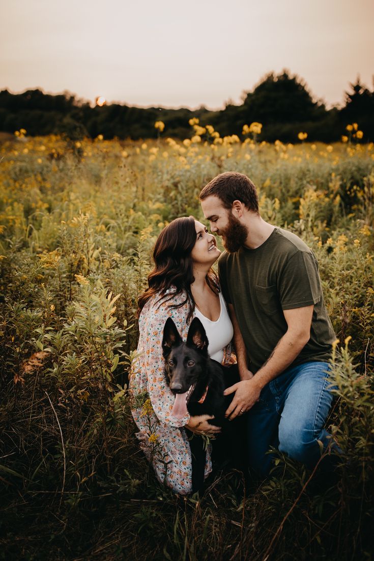 a man and woman kissing while holding a dog in a field full of tall grass