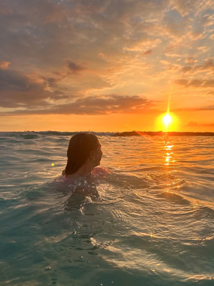 a woman swimming in the ocean at sunset with her head above the water's surface