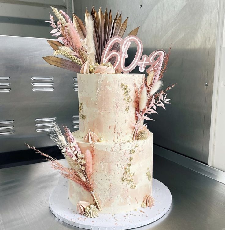 a three tiered cake decorated with feathers and flowers on a metal table in front of a microwave