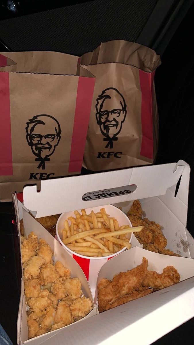 two boxes filled with chicken and fries next to bags of fried food on a table