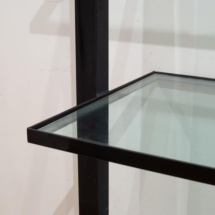 an empty glass shelf against a white wall with black metal frame and bottom part missing