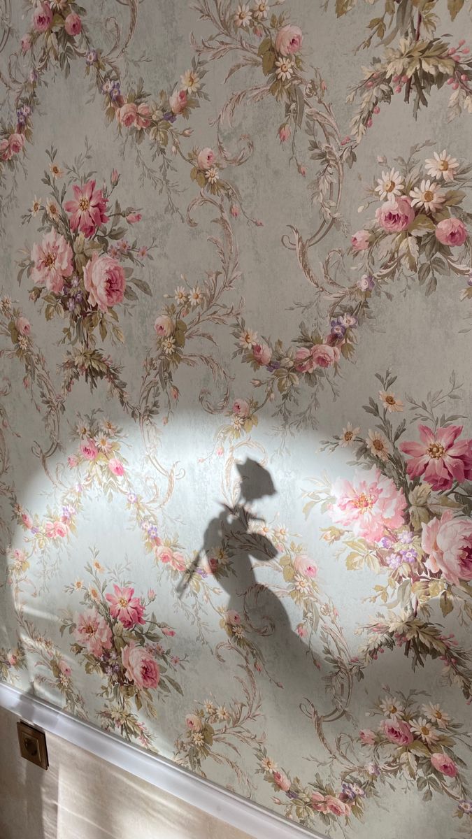 the shadow of a person holding an umbrella in front of a wall with flowers on it