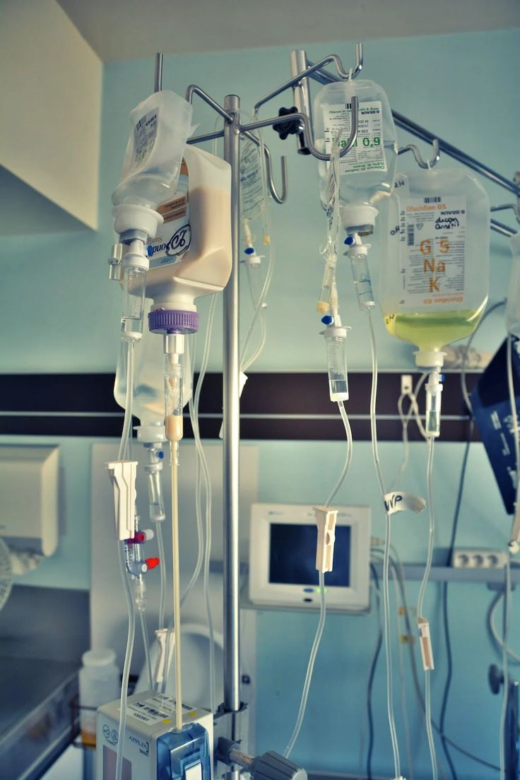 medical equipment in a hospital room with blue walls and ceiling lights, including monitors, ivs, and machines