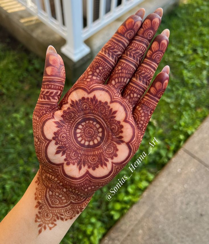 a hand with henna on it is shown in front of some grass and bushes