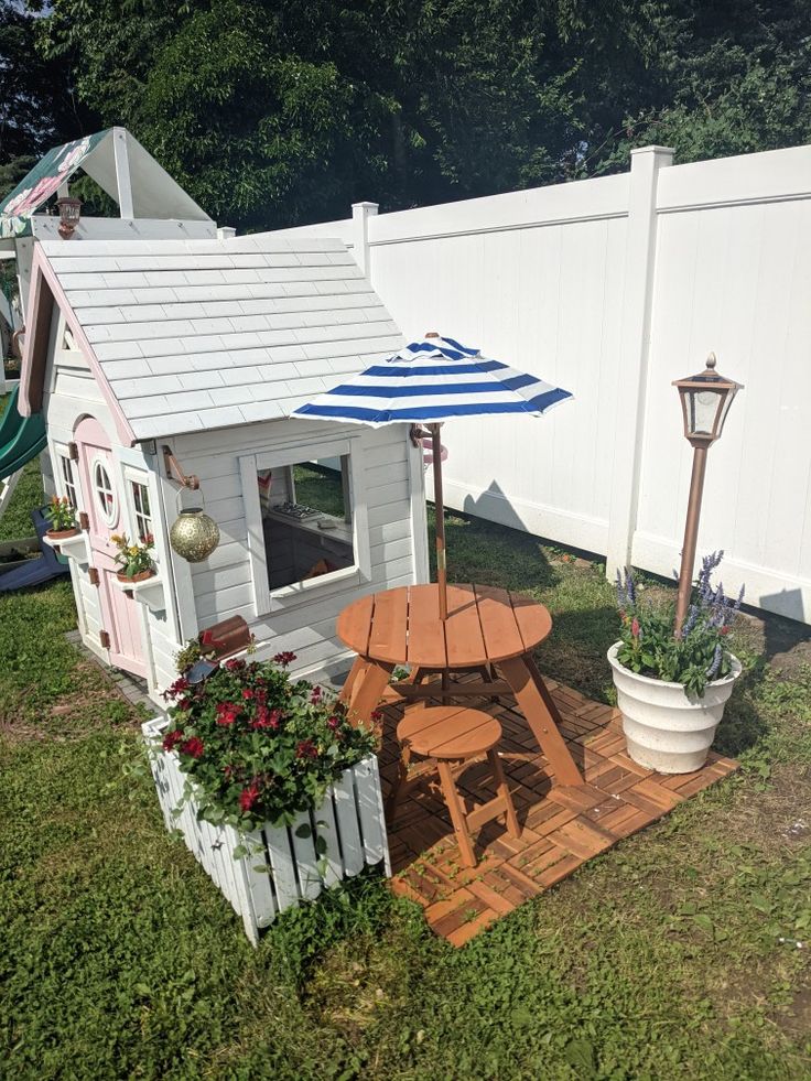 a small dog house with an umbrella over it's roof and flowers in the potted planter