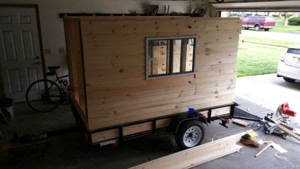 a tiny house built into the back of a trailer in a garage with tools on the floor