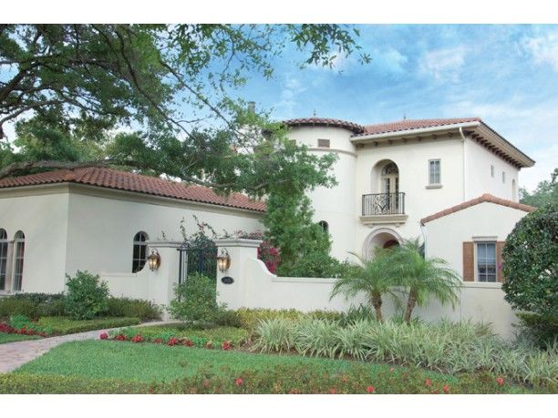 a white house with red tile roof and palm trees in the front yard, surrounded by greenery