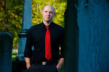 a man in a black shirt and red tie standing next to a cemetery with his hands on his hips