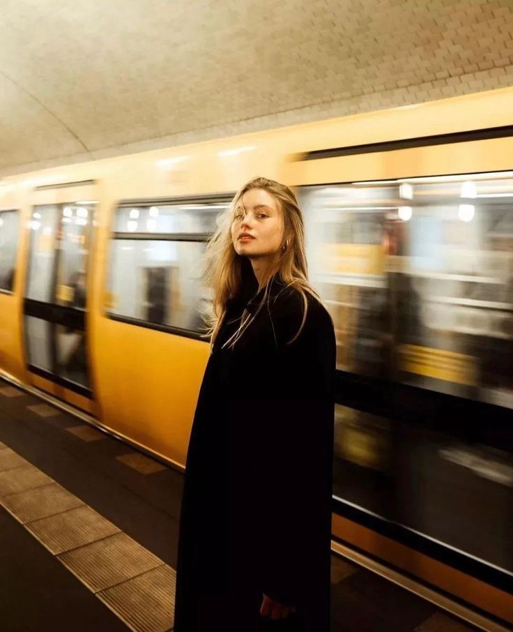 a woman standing in front of a train at a subway station with her head turned to the side