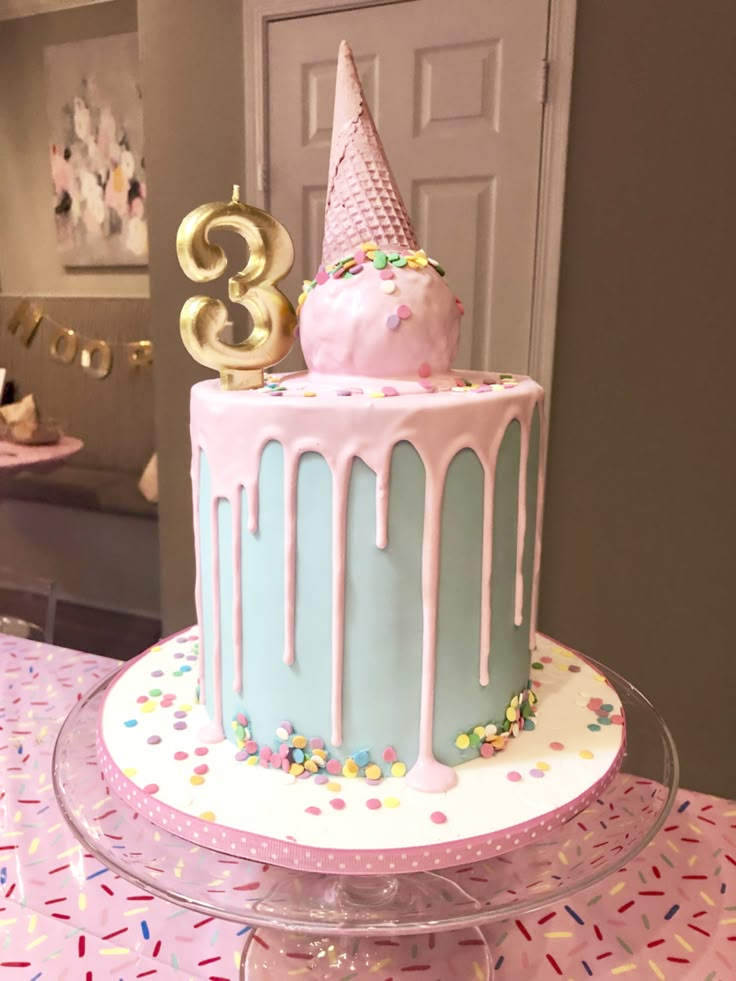 a pink and blue birthday cake with sprinkles on it sitting on a table