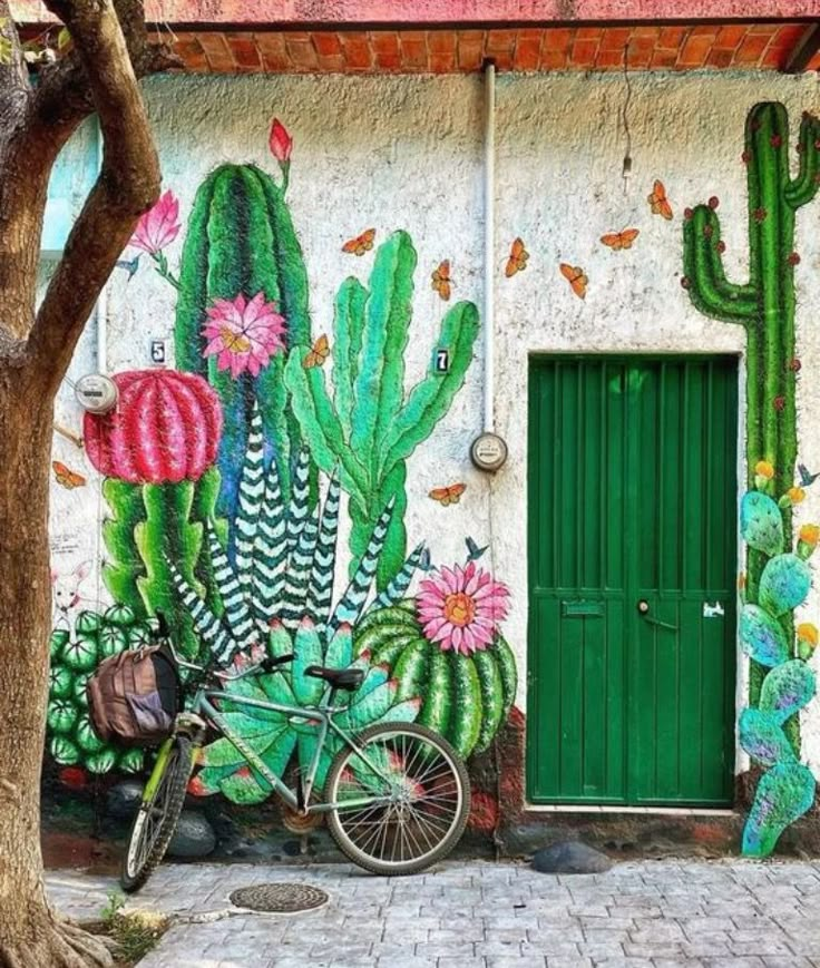 a bicycle parked in front of a building with cactus paintings on the wall and green door