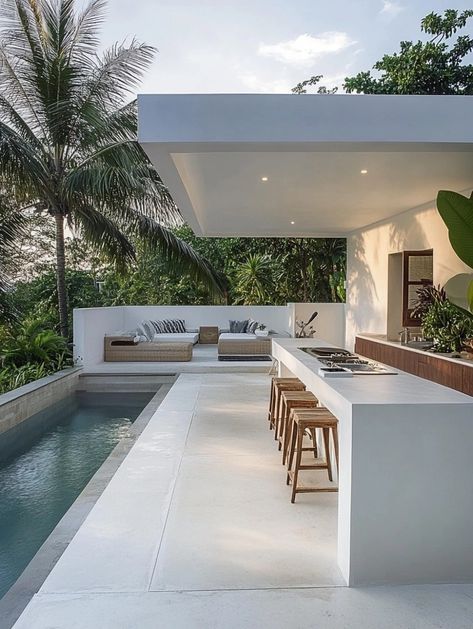 an outdoor kitchen next to a swimming pool with bar stools on the side and palm trees in the background