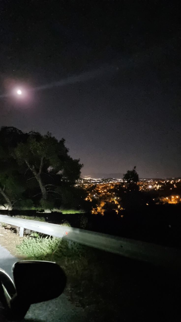 the car is parked on the side of the road at night with the moon in the background